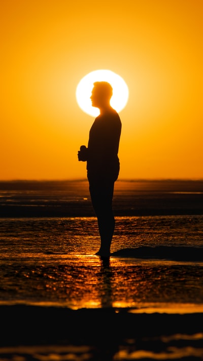 日落时分站在海滩上的男人的剪影